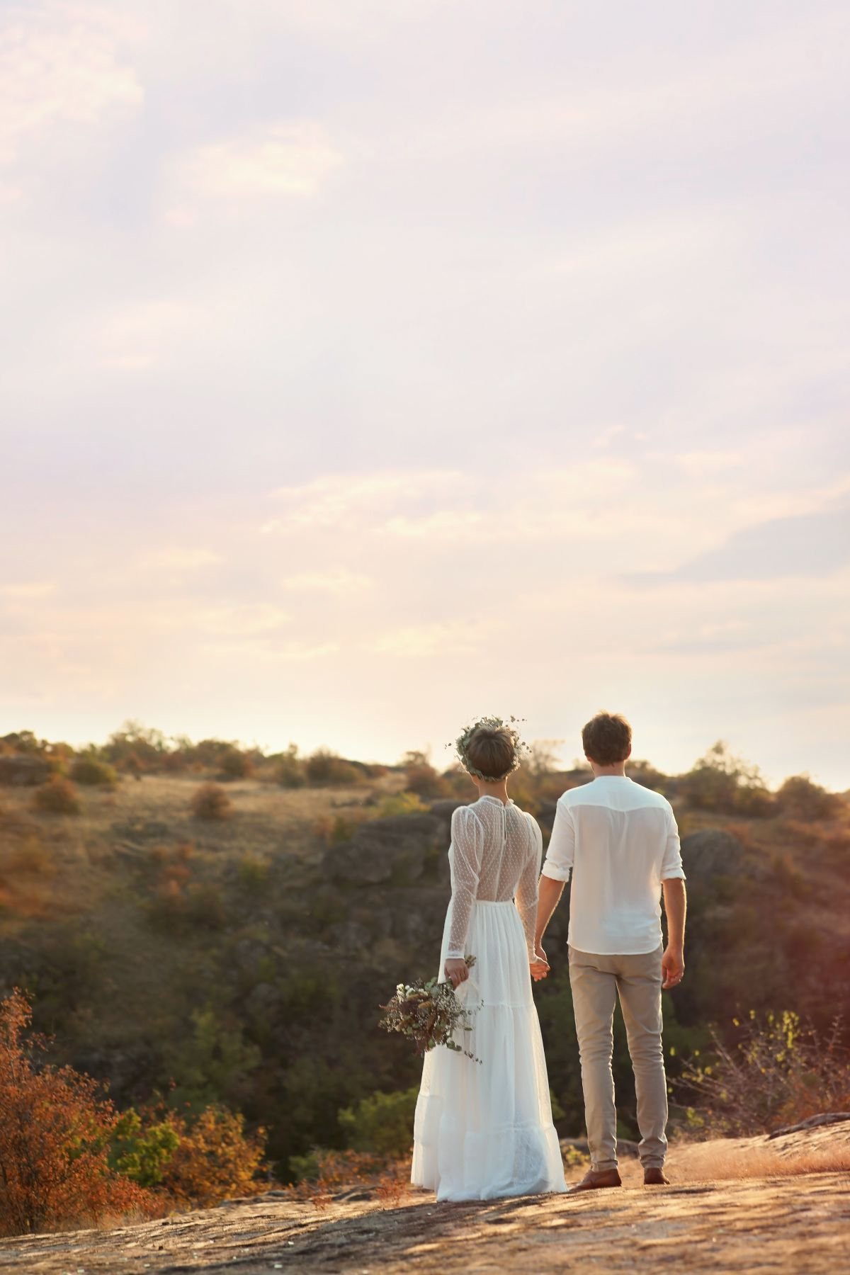 Couple holding hands on a rocky ridge, looking out over the hills at sunset
